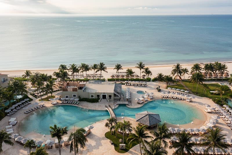 Aerial of a beachfront free-form pool lined with palms and cabanas at an adults-only all-inclusive resort in Riviera Maya, Mexico